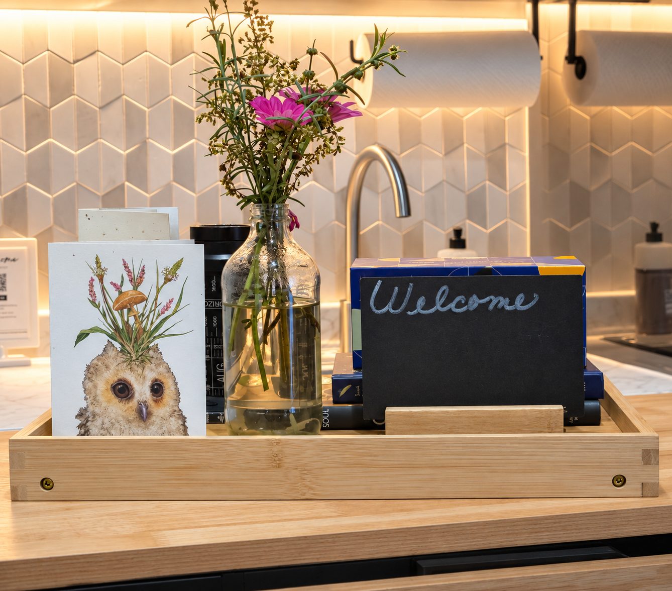 A welcome tray at Laurel & Lore: a hand-illustrated owl card, wild flowers in a glass bottle, and a small chalkboard reading Welcome